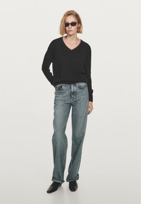 Zwarte v-halstrui, lichtblauwe hoge taille jeans, strakker rond de heupen, flared aan de onderkant, gecombineerd met zwarte enkellaarsjes.