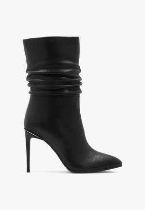 Melnas ādas potīšu zābaki ar noliekta dizaina, smailu pirkstu un augstu stiletto papēdi. Ietver diskretas spīduma un elegantu siluetu.