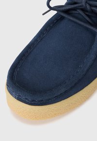 Blue suede upper shoe with round toe, stitched detailing, and a tan textured rubber sole. Features lace-up design and soft finish.