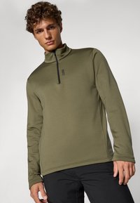 Suéter de manga larga en verde oliva con un alto collar y cremallera negra. Presenta un diseño minimalista con un sutil detalle de logo en el pecho.