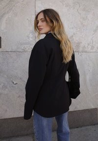 Must mängitud ülerõivastest bleiser, millel on struktureeritud õlad, kontrastiks helesinised teksad. Väike must käekott täiendab välja nägemist.