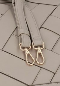 Details einer hellgrauen Lederhandtasche mit gewobener Textur, zwei verstellbaren Trägern und Beschlägen in Goldton, die klare Linien und Handwerkskunst hervorheben.