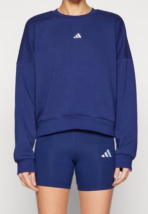 Osoba ubrana w niebieską bluzę z długim rękawem oraz dopasowane niebieskie szorty, oba z małym białym logo Adidas.