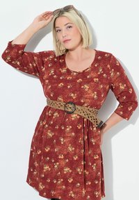 Rostfarbiges Kleid mit floralem Muster, Dreiviertelärmel und tailliertem Schnitt. Es hat einen gewebten beige Gürtel mit einer runden schwarzen Schnalle.
