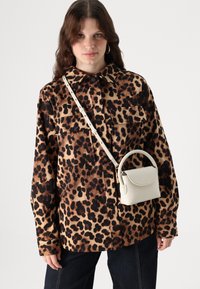 Camicia oversize con stampa leopardata e due tasche sul petto, abbinata a una piccola borsa a tracolla in pelle bianca con manico curvo.