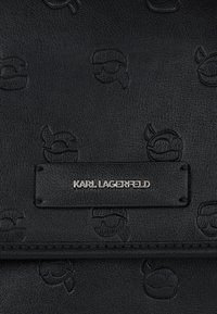 Čierna kožená kabelka s embosovanými vzormi loga Karl Lagerfeld, striebornou značkovou doskou, hladkým povrchom a čistými líniami.