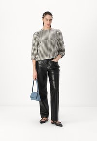 Blusa a scacchi bianca e nera con maniche a sbuffo, abbinata a pantaloni in pelle nera a vita alta. Tiene una piccola borsa blu e indossa ballerine nere.