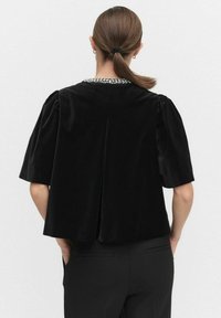 Czarny aksamitny top z krótkimi bufkami i rozcięciem z tyłu. Ozdobiony kołnierzykiem z metalicznymi akcentami. Gładka faktura i luźny fason.