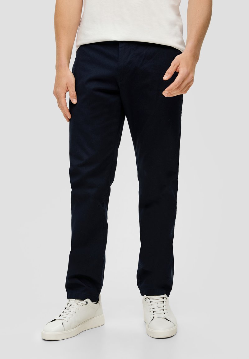Granatowe, proste spodnie chinos wykonane z bawełny, o gładkiej teksturze i bocznych kieszeniach. Noszone z białymi trampkami.