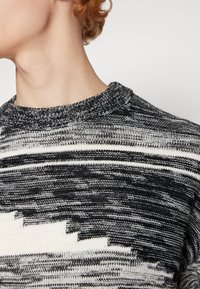 Maglione lavorato a maglia con un motivo astratto in bianco e nero, colletto rotondo, tessuto testurizzato e una vestibilità rilassata nel collo.