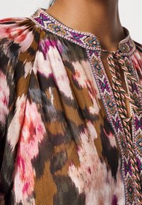 Painettu yläosa ruskean, vaaleanpunaisen ja vihreän sävyissä. Siinä on kirjailtu kaula-aukko värikkäillä korostuksilla ja avainaukko. Kevyt kangas.