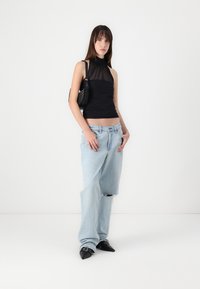 Black sleeveless top with sheer fabric, paired with light blue loose-fitting jeans featuring a ripped hem and pointed black shoes.