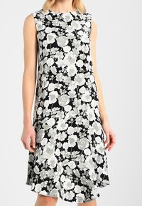 Černé šaty bez rukávů s květinovým vzorem v odstínech šedé a bílé, volného střihu a rozšířeným lemem. Měkká textilie.