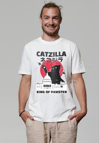 Ein weißes Baumwoll-T-Shirt mit einem grafischen Design einer schwarzen Katze vor einem roten Kreis, mit dem Text "CATZILLA" und "KING OF PAWSTER" darunter.