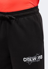 Μαύρη φόρμα Puma με ελαστική μέση και κορδόνι, με λευκή και γκρι επιγραφή "CREW 748" και λογότυπο στον αριστερό μηρό.