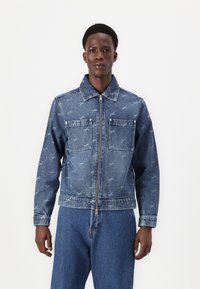 Denim jacket in light blue with a subtle pattern, featuring two front pockets, a zip closure, and a classic collar. Smooth texture.