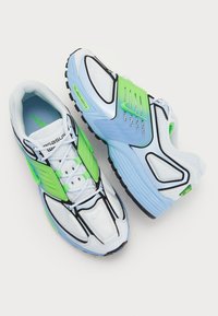 Scarpe da ginnastica bianche e blu con accenti verdi, materiale in mesh, suola testurizzata e un design delineato in nero con marchio distintivo.