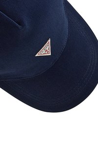 Mörkblå keps gjord av tyg, med en triangulär röd och vit "Guess" logotypapplikation på framsidan. Slät textur, strukturerad design.