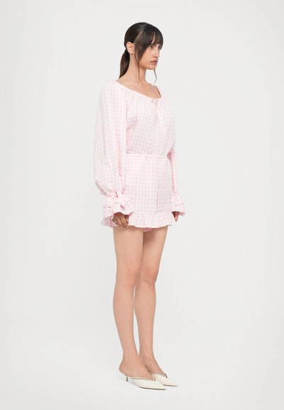 Rožinė gingham suknelė su pūstomis rankovėmis, elastinga juosmeniu ir raukšlėta apatine dalimi. Lengvas audinys suteikia švelnią tekstūrą.