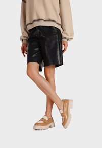 Sweatshirt beige, pantaloni in pelle nera, e scarpe platform beige con suola spessa e dettagli in cinturino. Texture lisce e design moderno.