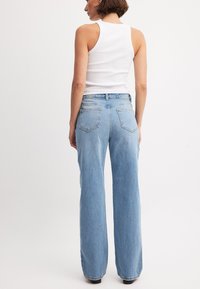 Vaaleansiniset korkeavyötäröiset farkut, joissa on rento leikkaus, pehmeä denimituntu ja kaksi takaosataskua, yhdistettynä valkoiseen hihattomaan toppiin.