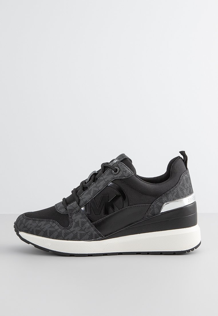 Zwarte sportieve sneaker van textuurstof, met leren accenten en een zilveren logo-detail. Heeft een dikke witte zool en contrasterende patronen.