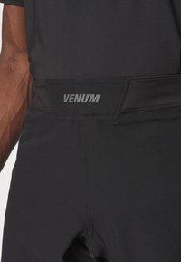 Schwarze Sporthosen mit glatter Textur, ausgestattet mit einem breiten Bund und einem auffälligen VENUM-Logo in Silber.