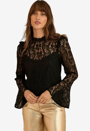 Schwarze Spitzenbluse mit langen Ärmeln und ausgestellt geschnittenen Manschetten, hohem Kragen mit Rüschendetails und kunstvollen Blumenmustern.
