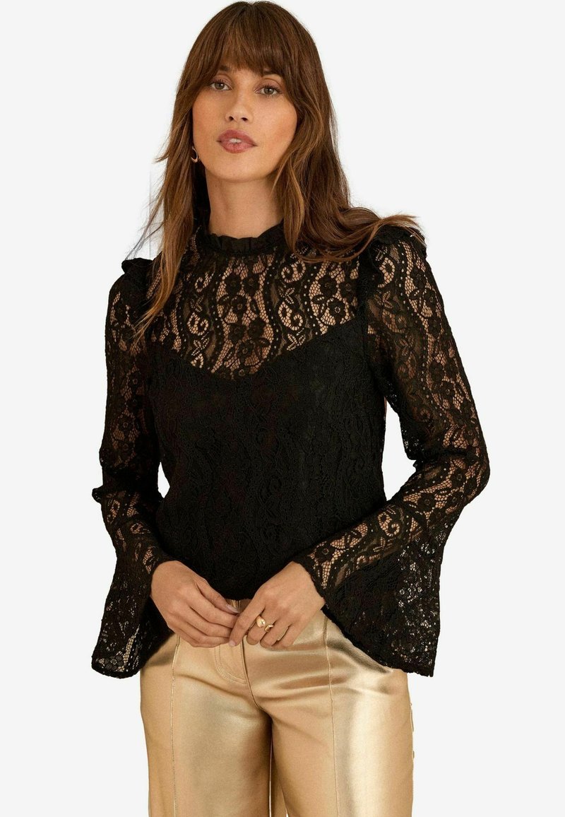 Blusa nera in pizzo con maniche lunghe a campana, collo alto con dettagli arricciati e motivi floreali intricati.