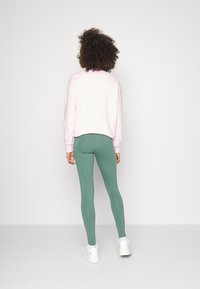 Jasnoróżowy cropped sweatshirt w połączeniu z zielonymi legginsami. Legginsy mają gładką fakturę i są dopasowane do sylwetki, wykończone białymi sneakersami.