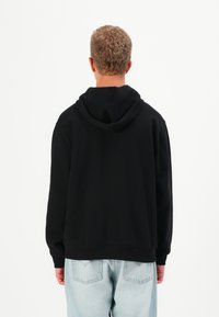 Black hoodie with a drawstring hood, ribbed cuffs and hem, worn with light blue jeans. Simple design, no visible patterns or logos.