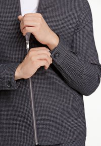 Grå zip-up jacka med rutigt mönster, som har en mjuk textur, knäppta manschetter och en silverfärgad dragkedja.