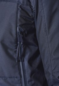 dunkelblaue Jacke aus Stoff mit strukturiertem Oberflächen, ausgestattet mit einer Reißverschlusstasche und Zugbanddetails an der Seite für eine verstellbare Passform.