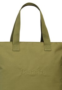 Olijfgroene stoffen draagtasje met twee stevige hengsels en het ingedrukte "Bench." logo aan de voorkant. Gladde textuur en rechthoekige vorm.