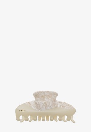 Pince à cheveux en plastique beige et marbré avec des dents courbées et un petit logo métallique sur un côté.