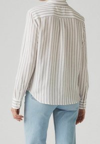 Chemise à manches longues rayée en tissu léger avec des rayures verticales blanches et foncées, présentant un poignet à boutons et un ourlet courbé.