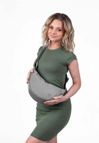 Šedá, zakřivená, polstrovaná taška přes tělo vyrobená z hladkého materiálu. Nastavitelný popruh, držená v rukou, v kombinaci se zelenými přiléhavými šaty. Jednoduchý, moderní design.