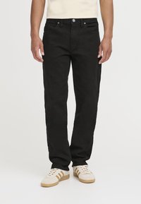 Sorte denimjeans med rett passform, fem lommer og metallknapp. Brukt med beige joggesko.