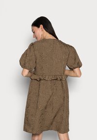 Vestido castanho texturizado com mangas bufantes, cintura com babados e padrões florais. A vista traseira mostra detalhes de costura e decote.