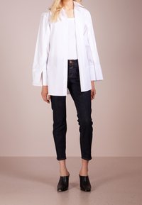 Bílá košile s dlouhými rukávy, spárovaná s tmavými slim fit džíny a černými vysokými mules. Jednoduchý, čistý design.