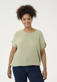 Hellgrünes, kurzärmliges Bluse mit lässiger Passform und subtiler Textur. Kombiniert mit dunkelblauen Jeans. Einfacher runder Ausschnitt.