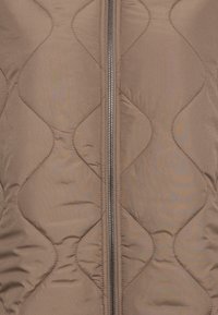 Brun vadderad väst med diamantmönster, med en central dragkedja och en slät, glänsande tygtextur.