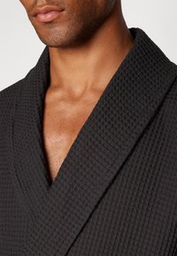 Black waffle-textured bathrobe with a wide collar, showing a close-up of the neckline and skin tone beneath. No visible embellishments.