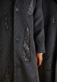 Palton gri din lână, cu patch-uri decorative cu model în zigzag, fixat cu elemente de tip cârlig și ochi, și închidere clasică cu nasturi.