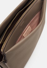 Braune Lederhandtasche mit goldenem Reißverschluss, ausgestattet mit einer glatten Textur. Innen hat sie ein rosa Satinfutter und ein Etikett, das italienisches Leder beschreibt.