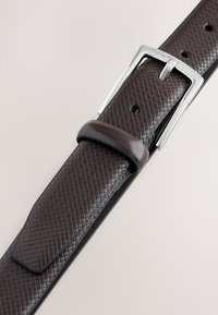 Hnedý kožený opasok s textúrou v tvare diamantového vzoru, vybavený striebornou obdĺžnikovou prackou a prislúchajúcou koženou slučkou.