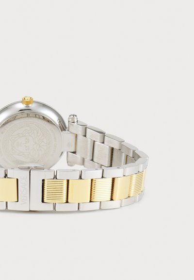 Silver and gold-toned metal watch with a round face, textured bracelet, and a yellow crown; back features a detailed logo design.