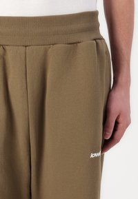 Braune Baumwoll-Sweatpants mit elastischem Bund und weißen Logodetails, ausgestattet mit Seitentaschen und einer weichen, glatten Textur.