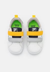 Sneaker bianche con accenti grigi, gialli e blu navy. Presentano cinturini in Velcro, forma arrotondata e una soletta verde dei Looney Tunes.
