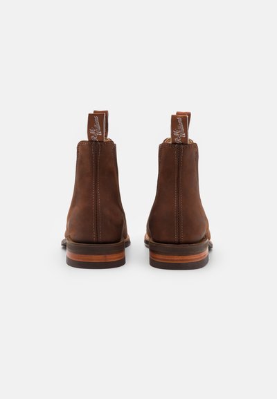 Botas de tobillo de cuero marrón con un acabado suave, refuerzo en la parte trasera y un tacón estratificado de color marrón claro que contrasta. Las lengüetas en la parte superior cuentan con costuras con la marca.